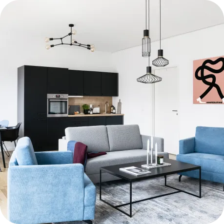 Ein modernes, offenes Wohnzimmer mit Küche im minimalistischen Stil. Hellblaue Sessel, ein graues Sofa und schwarze Akzente sorgen für eine ruhige, stilvolle Atmosphäre. Hängelampen und abstrakte Wandkunst verleihen dem Raum zeitgemäßen Charakter.