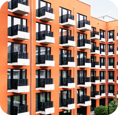 Leuchtend orangefarbenes Wohngebäude mit mehreren Etagen, auf denen sich kleine weiße Balkone mit schwarzen Geländern befinden. Die moderne Fassade wirkt lebendig und einheitlich.