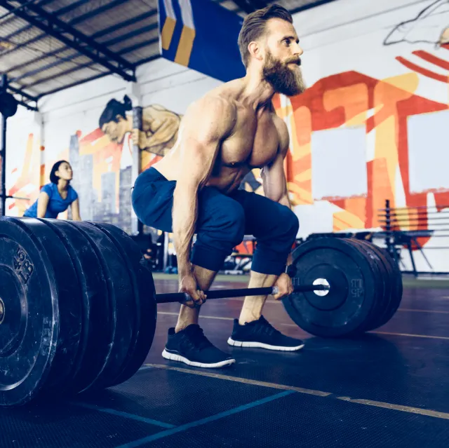 Muskulöser Mann macht ein schweres Kreuzheben in einem Fitnessstudio mit bunter Graffiti-Wand.