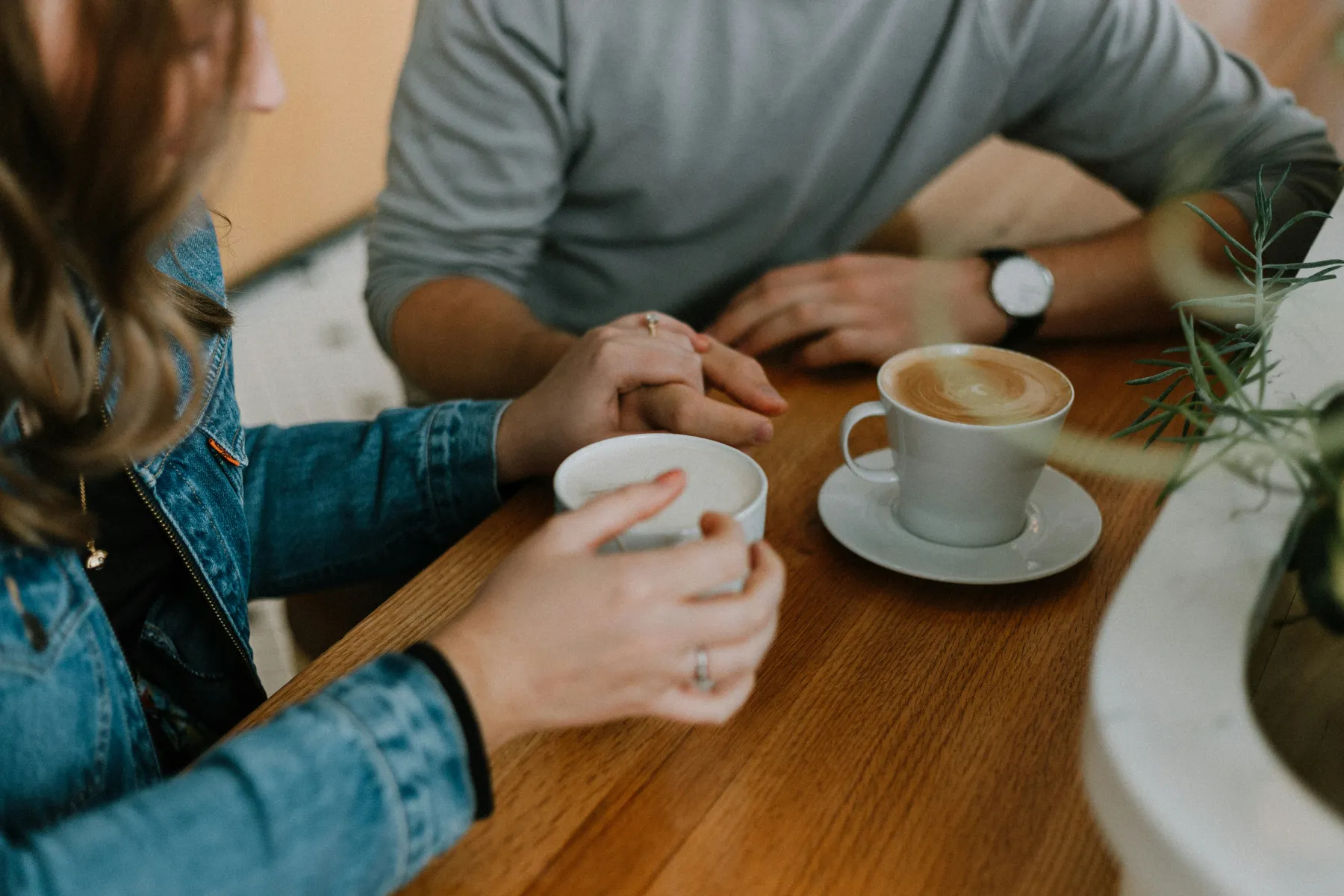 A couple holding hands over coffee cups at a wooden table, captured in a cozy, intimate setting.