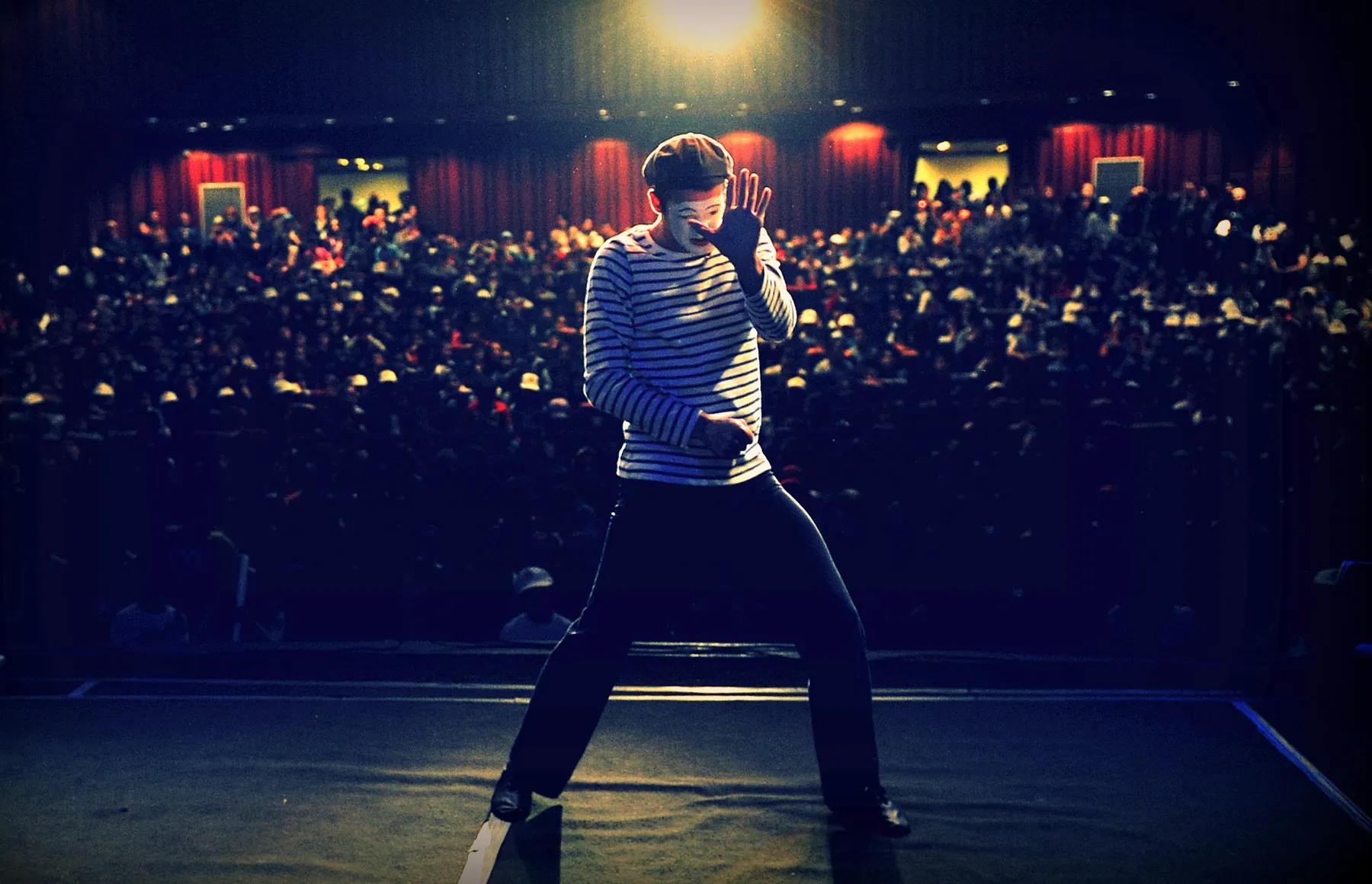 A mime performing on a brightly lit stage in front of a large audience.